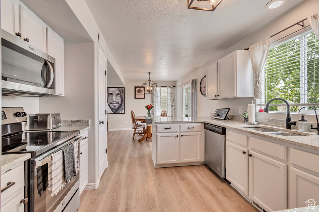 Kitchen featuring appliances with stainless steel finishes, a sink, a chandelier, light wood finished floors, and a peninsula