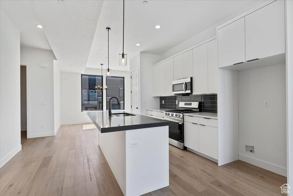 Kitchen featuring stainless steel appliances, a sink, a kitchen island with sink, light wood finished floors, and recessed lighting