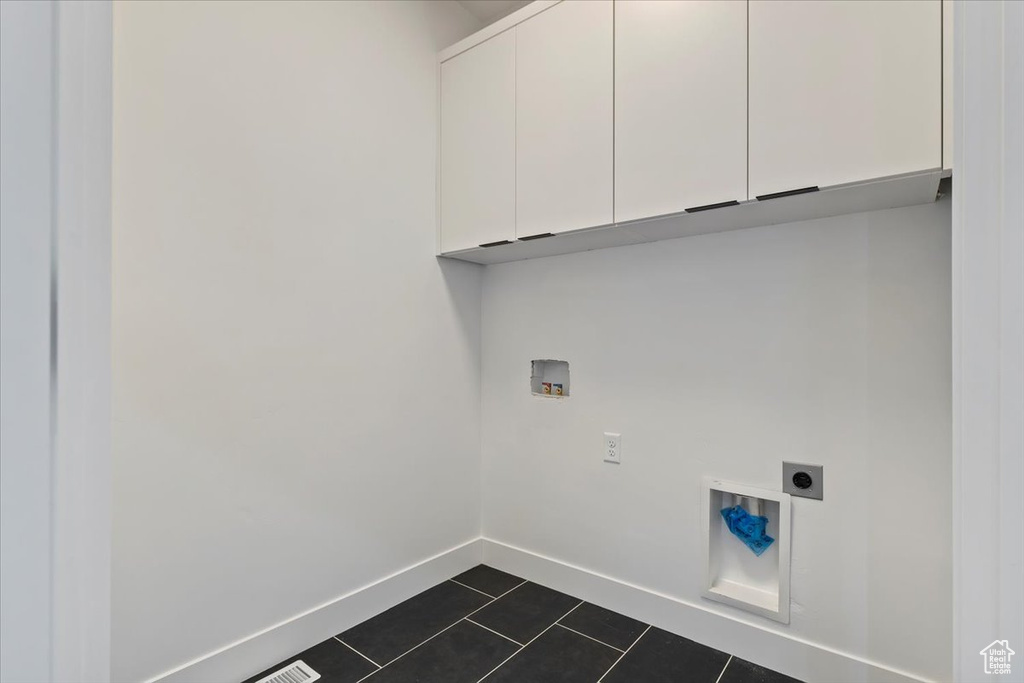 Laundry area with cabinet space, electric dryer hookup, hookup for a washing machine, dark tile patterned flooring, and baseboards