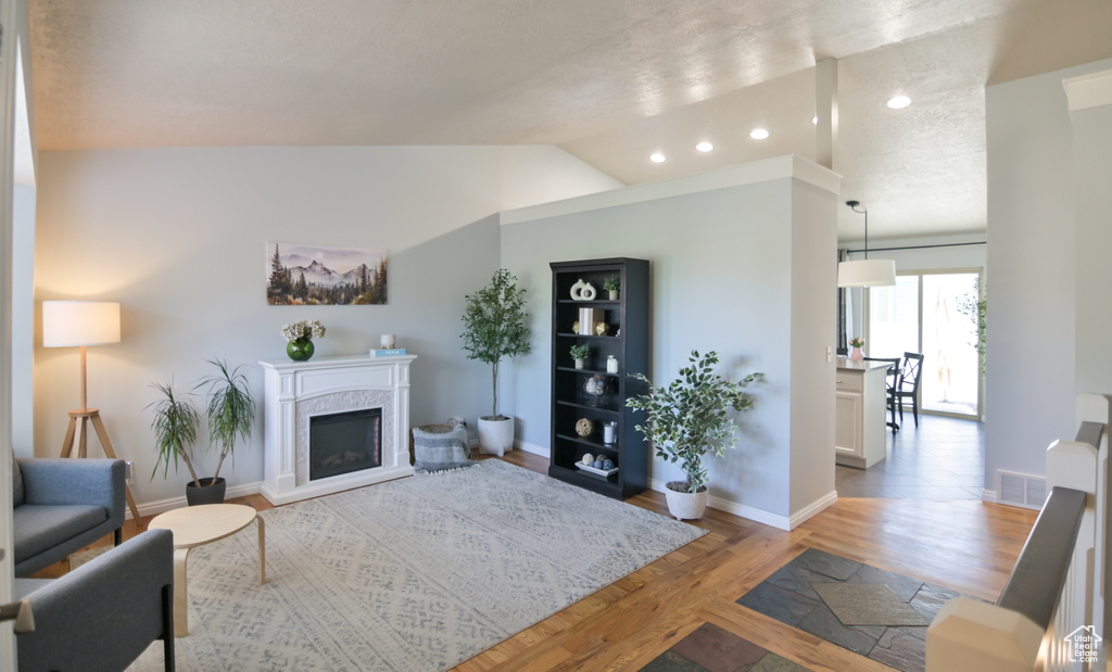 Living area featuring light wood-style flooring, a premium fireplace, baseboards, vaulted ceiling, and recessed lighting