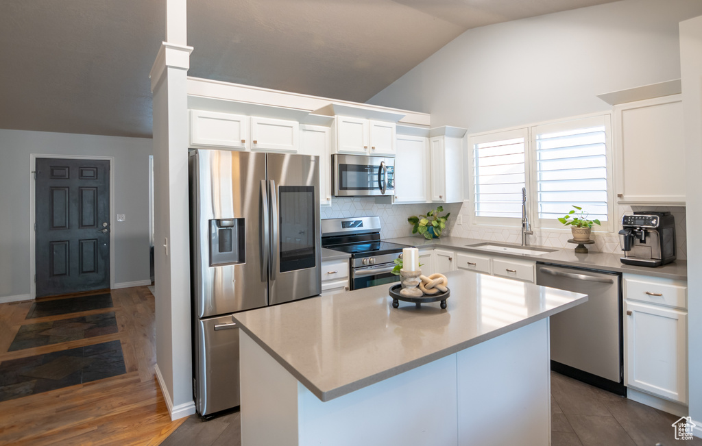 Kitchen featuring appliances with stainless steel finishes, a sink, vaulted ceiling, tasteful backsplash, and a center island