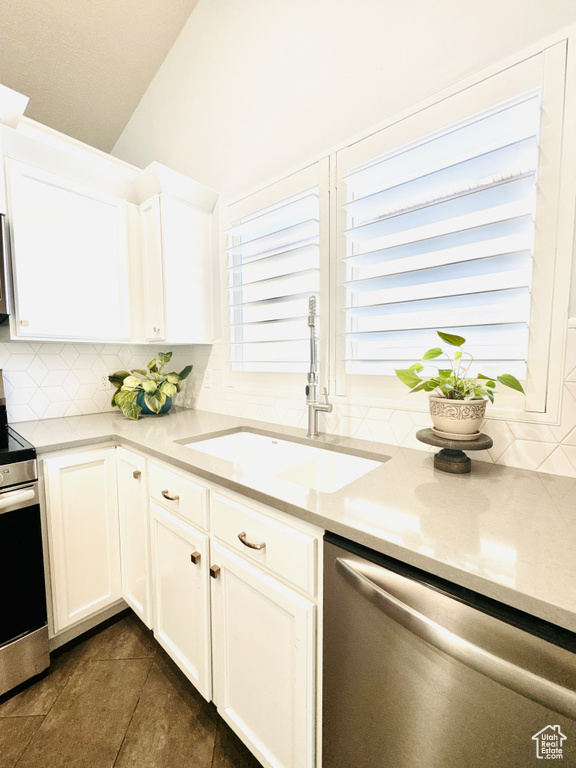 Kitchen featuring stainless steel appliances, a sink, tasteful backsplash, dark tile patterned floors, and white cabinetry