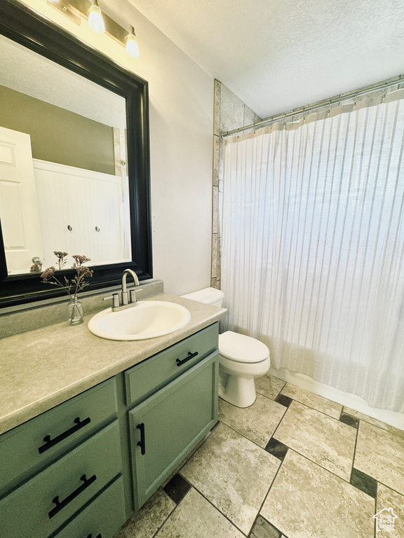 Full bath with vanity, toilet, stone tile floors, and a textured ceiling