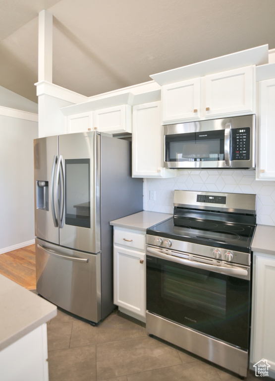 Kitchen with appliances with stainless steel finishes, tasteful backsplash, white cabinetry, and lofted ceiling