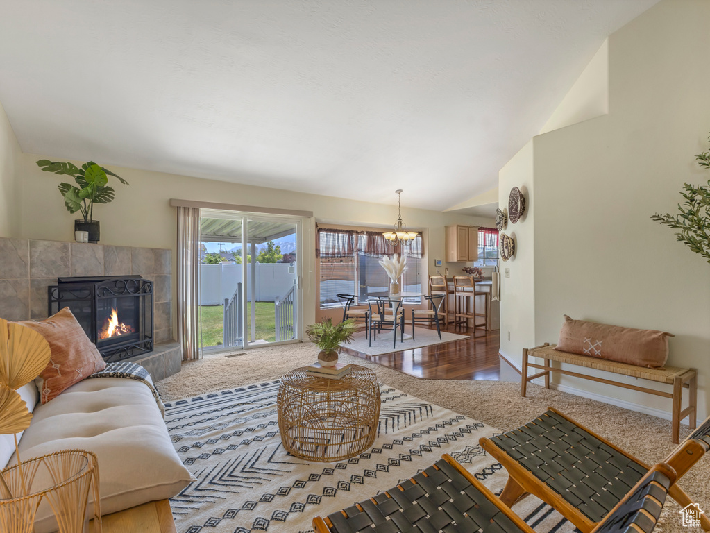 Living room featuring a tiled fireplace, vaulted ceiling, wood finished floors, and a chandelier
