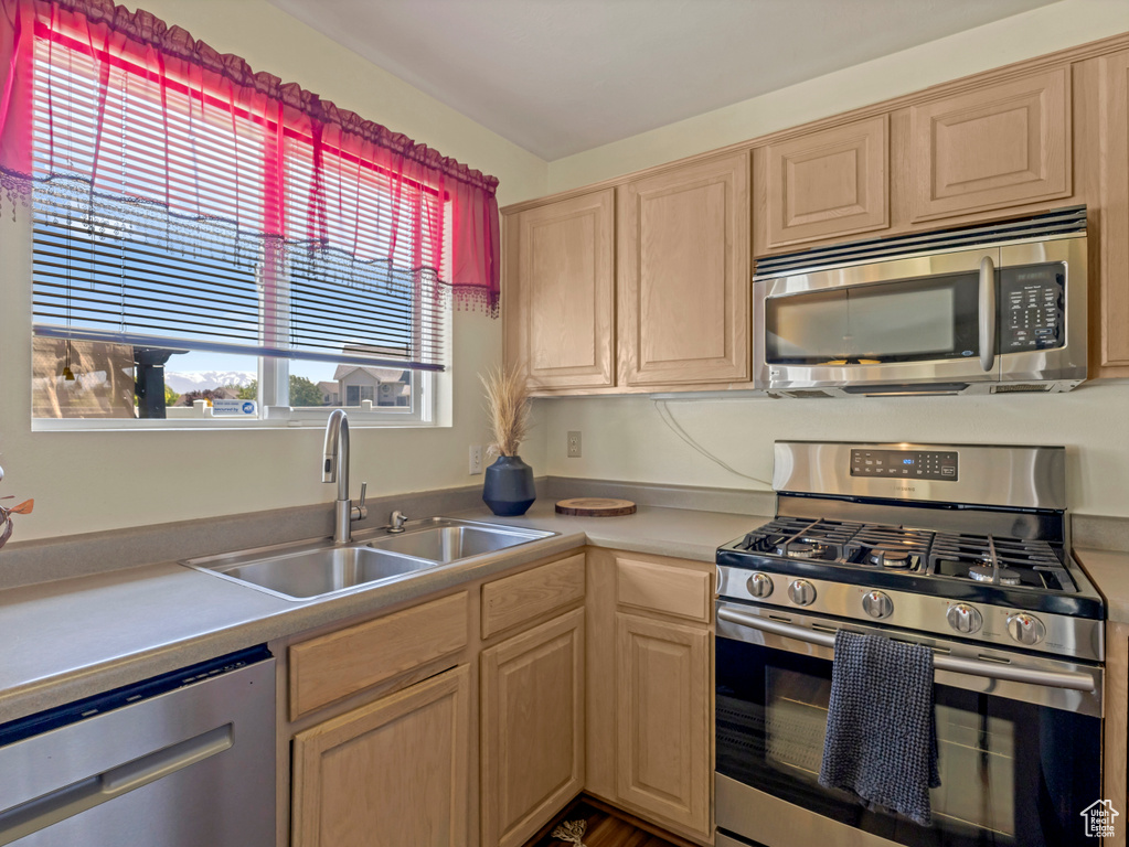 Kitchen with stainless steel appliances, a sink, light brown cabinets, and light countertops