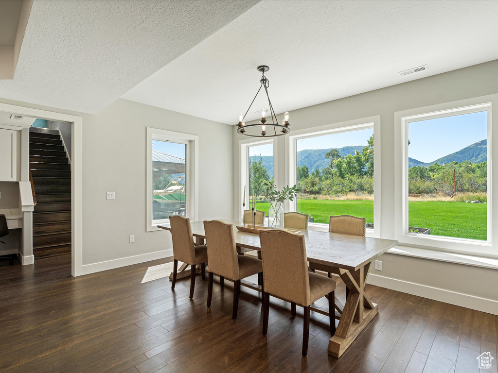 Dining room with a chandelier, baseboards, dark wood-style flooring, a mountain view, and stairway