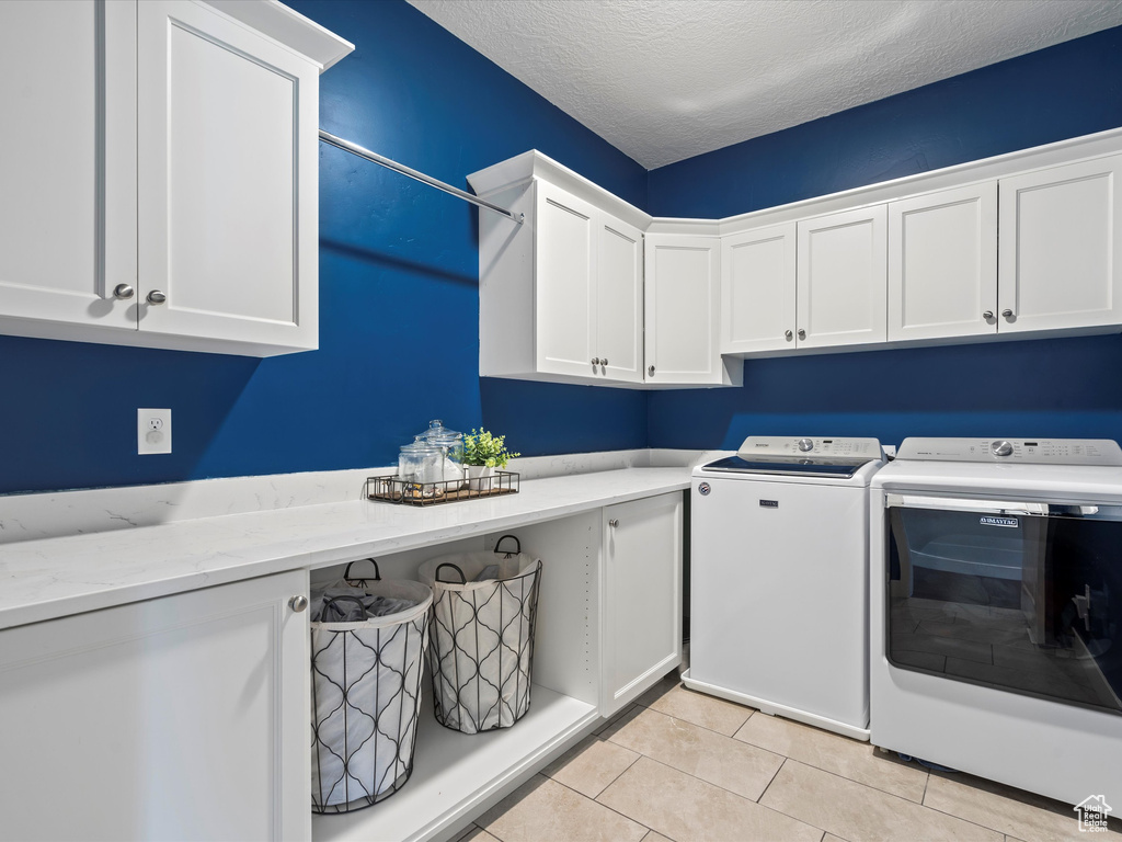 Clothes washing area with cabinet space, washing machine and dryer, light tile patterned flooring, and a textured ceiling