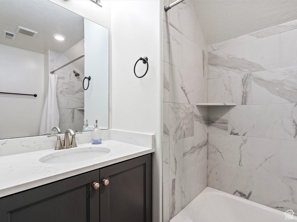Bathroom with a textured ceiling, vanity, and shower / tub combo