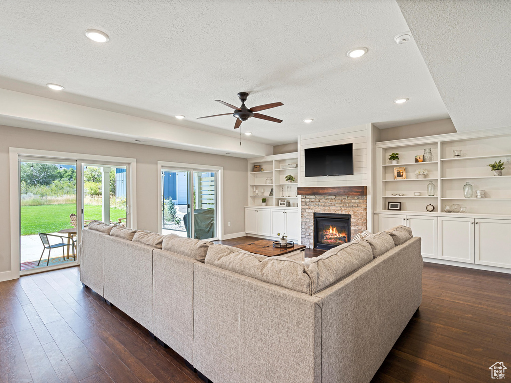 Living area featuring a textured ceiling, dark wood finished floors, baseboards, ceiling fan, and a fireplace
