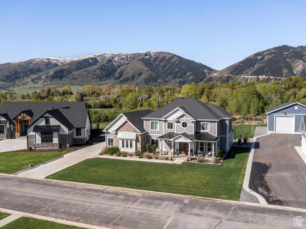 View of front facade featuring a mountain view, a detached garage, board and batten siding, a front lawn, and asphalt driveway