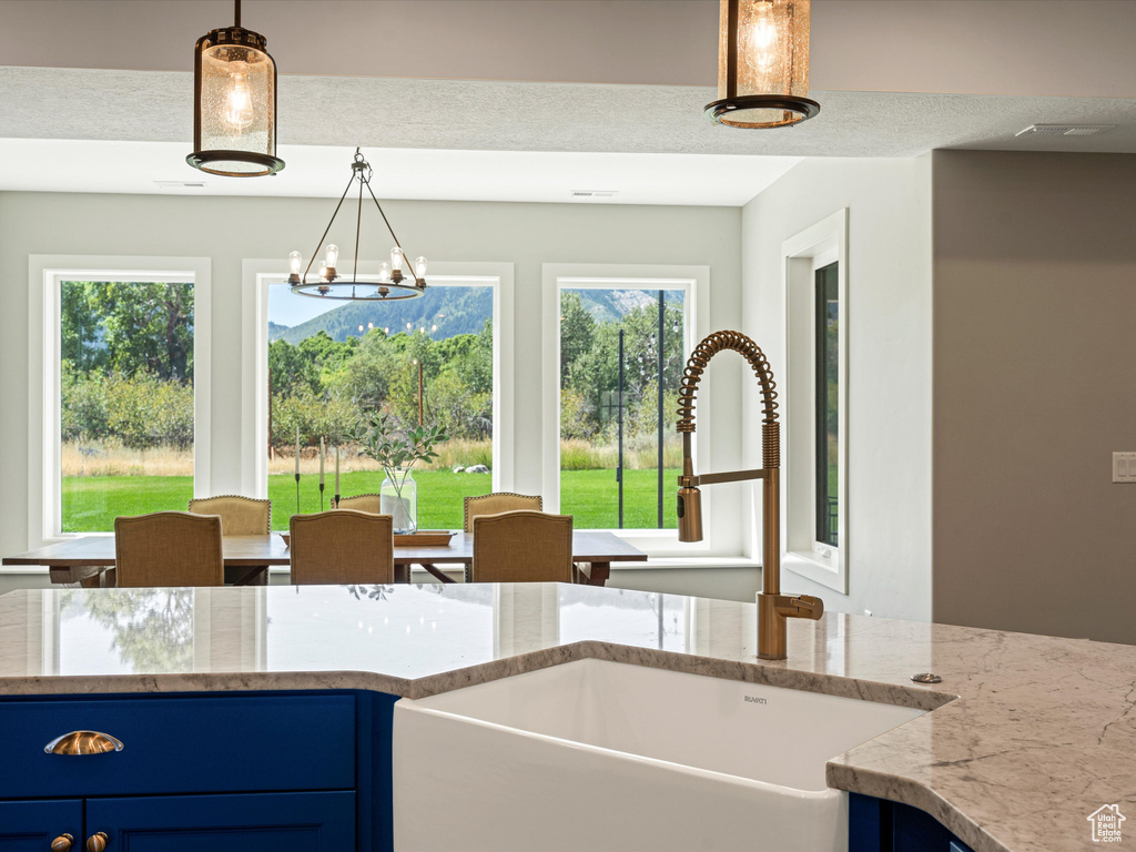 Kitchen featuring a sink, blue cabinetry, light stone countertops, pendant lighting, and a chandelier
