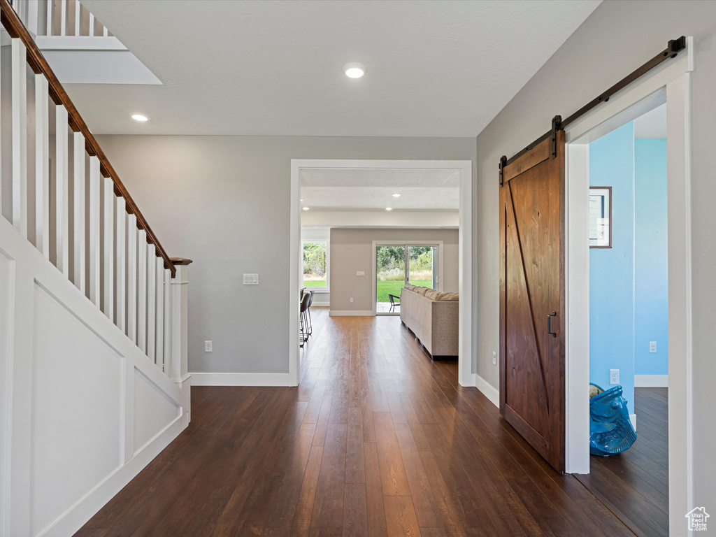 Entrance foyer with a barn door, dark wood-style floors, baseboards, stairs, and recessed lighting