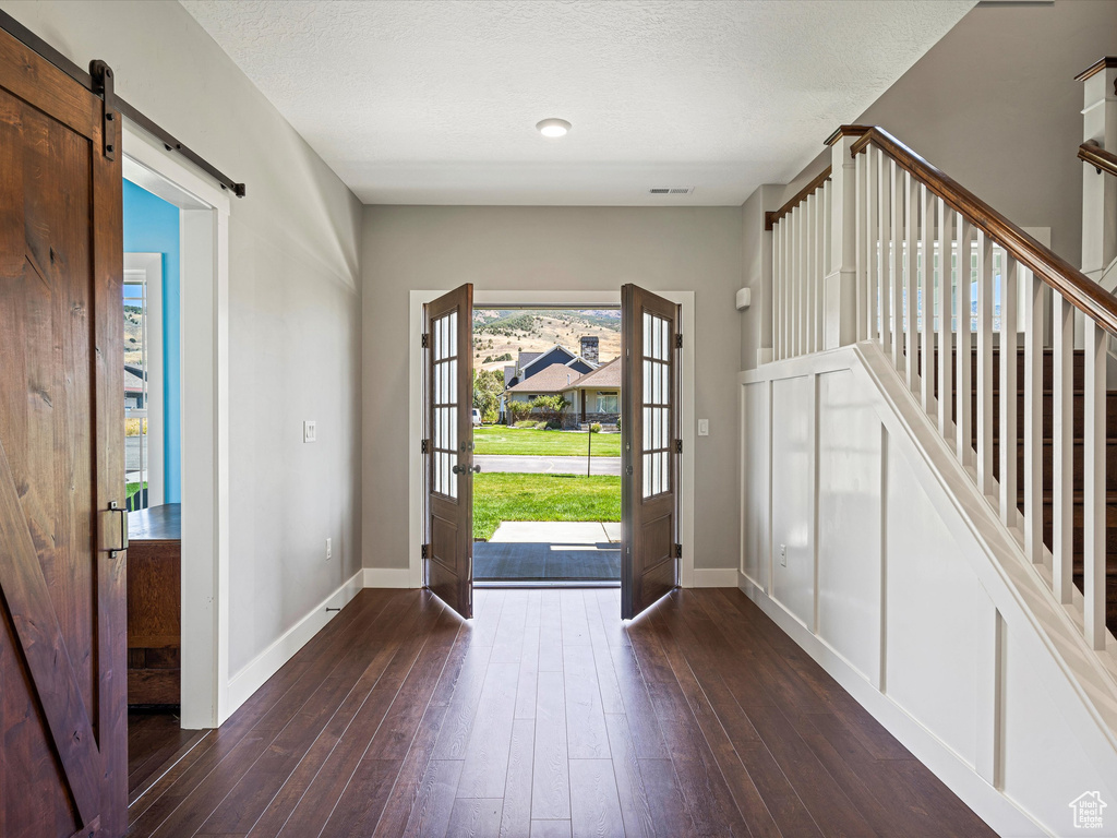 Entrance foyer featuring baseboards, dark wood-type flooring, a barn door, and a textured ceiling