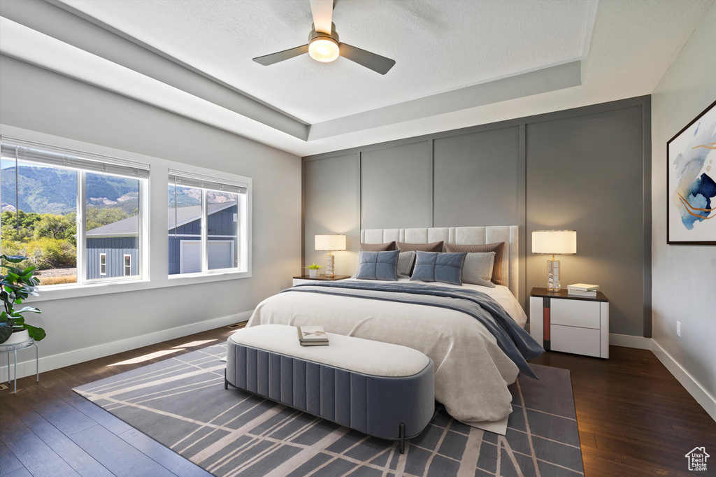 Bedroom with a tray ceiling, wood-type flooring, baseboards, and a ceiling fan