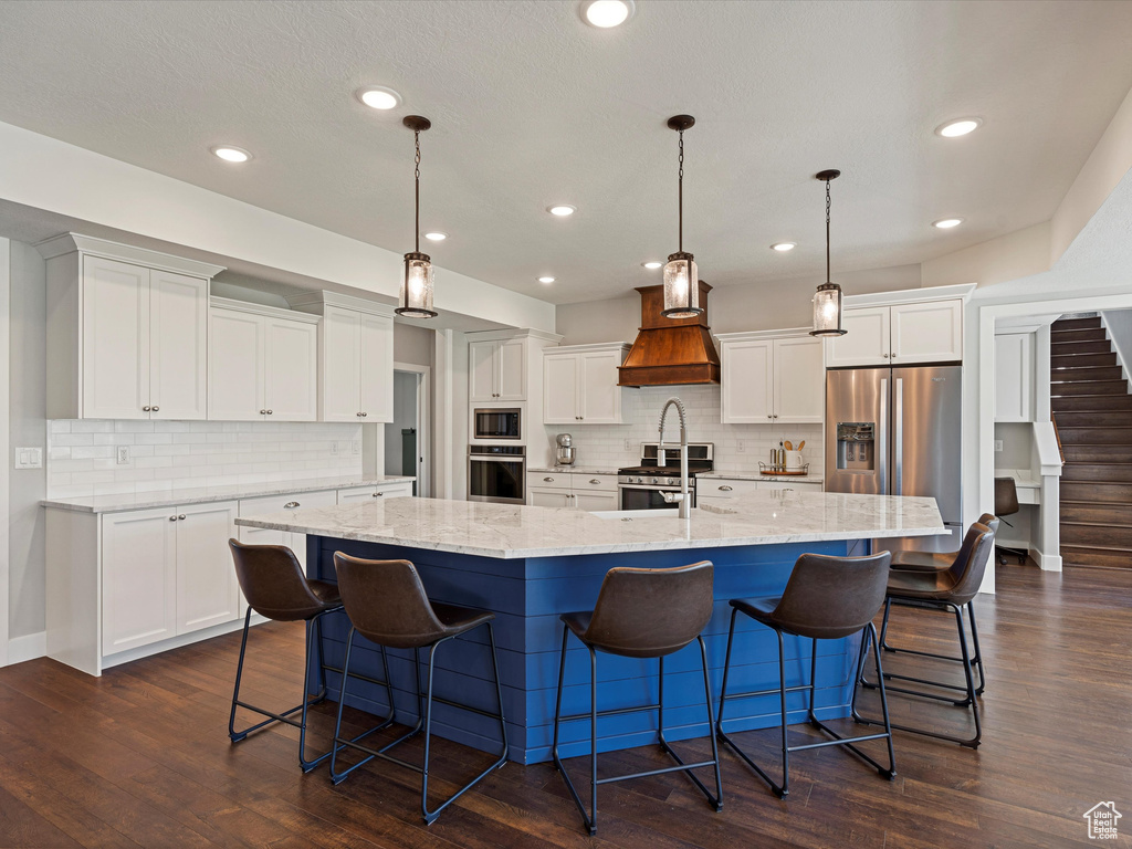 Kitchen with stainless steel appliances, custom exhaust hood, a large island, white cabinets, and decorative backsplash