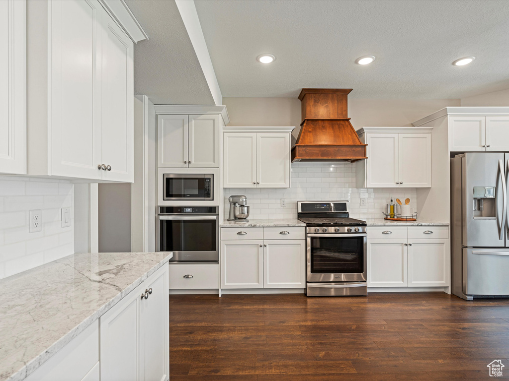 Kitchen featuring appliances with stainless steel finishes, custom range hood, decorative backsplash, white cabinets, and recessed lighting