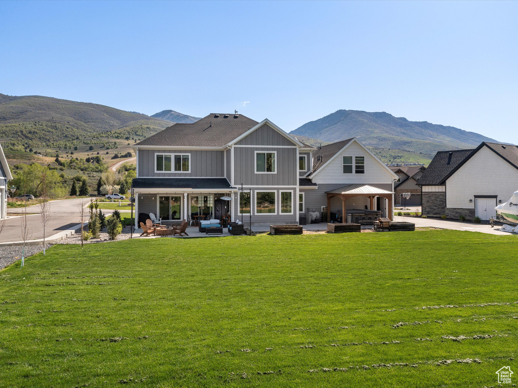 Back of property with board and batten siding, a patio area, a mountain view, and a lawn