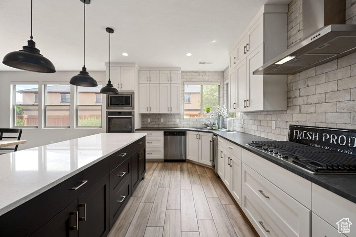 Kitchen with wall chimney range hood, stainless steel appliances, dark cabinets, white cabinetry, and decorative backsplash