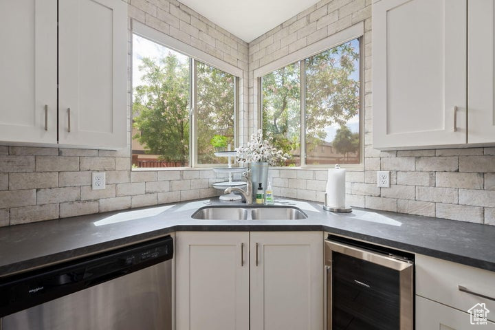 Kitchen with dishwasher, wine cooler, a sink, white cabinets, and decorative backsplash