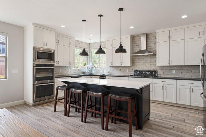 Kitchen featuring wall chimney exhaust hood, stainless steel appliances, light wood finished floors, healthy amount of natural light, and recessed lighting