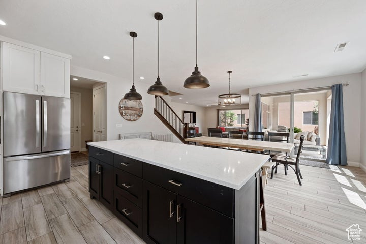 Kitchen featuring freestanding refrigerator, dark cabinets, white cabinets, light wood finished floors, and light countertops
