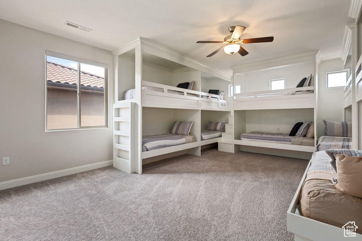 Carpeted bedroom with multiple windows, baseboards, ornamental molding, and ceiling fan
