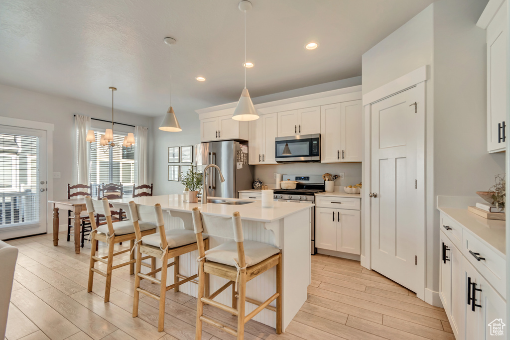 Kitchen featuring appliances with stainless steel finishes, a sink, light wood-type flooring, an island with sink, and a kitchen breakfast bar