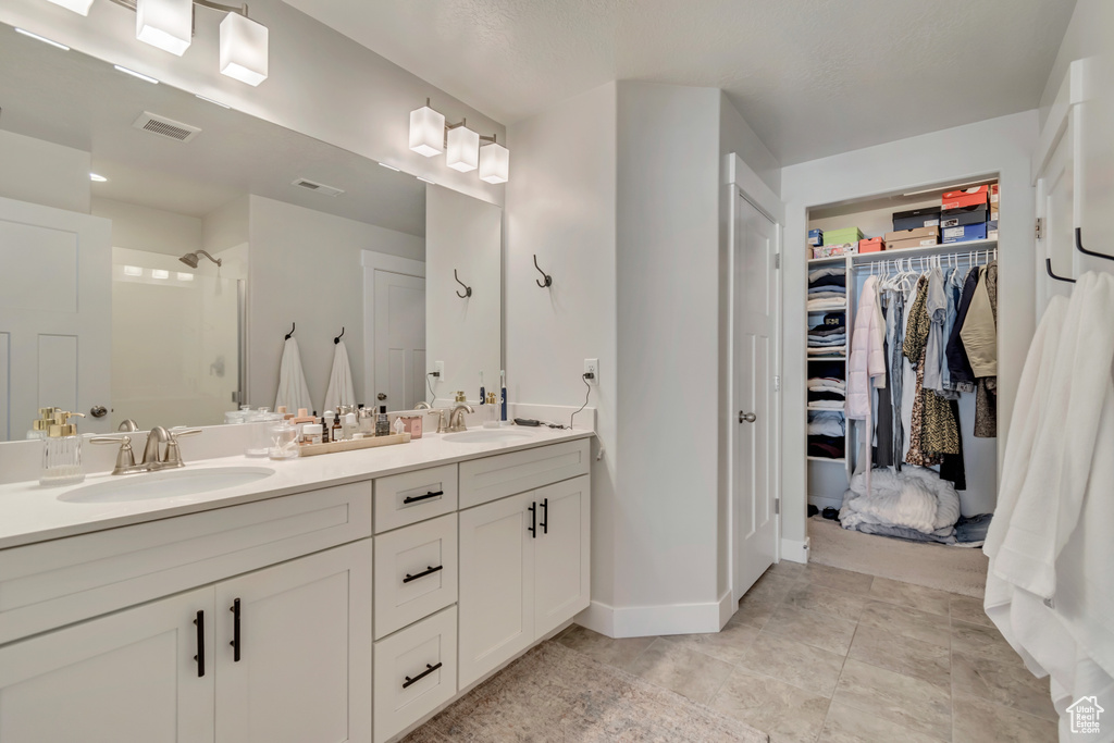 Bathroom featuring a shower stall, a spacious closet, double vanity, and baseboards