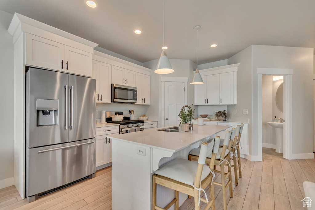 Kitchen with appliances with stainless steel finishes, a sink, light wood-style flooring, white cabinets, and recessed lighting