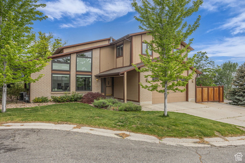 View of front facade featuring concrete driveway, an attached garage, central air condition unit, and brick siding
