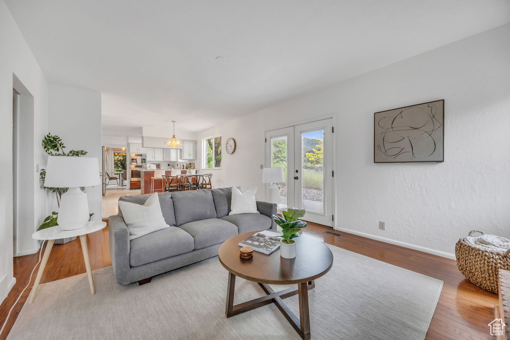 Living room with light wood finished floors, baseboards, french doors, and a chandelier