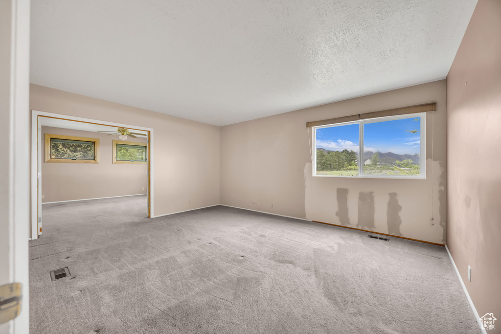 Carpeted spare room featuring baseboards, a ceiling fan, and a textured ceiling