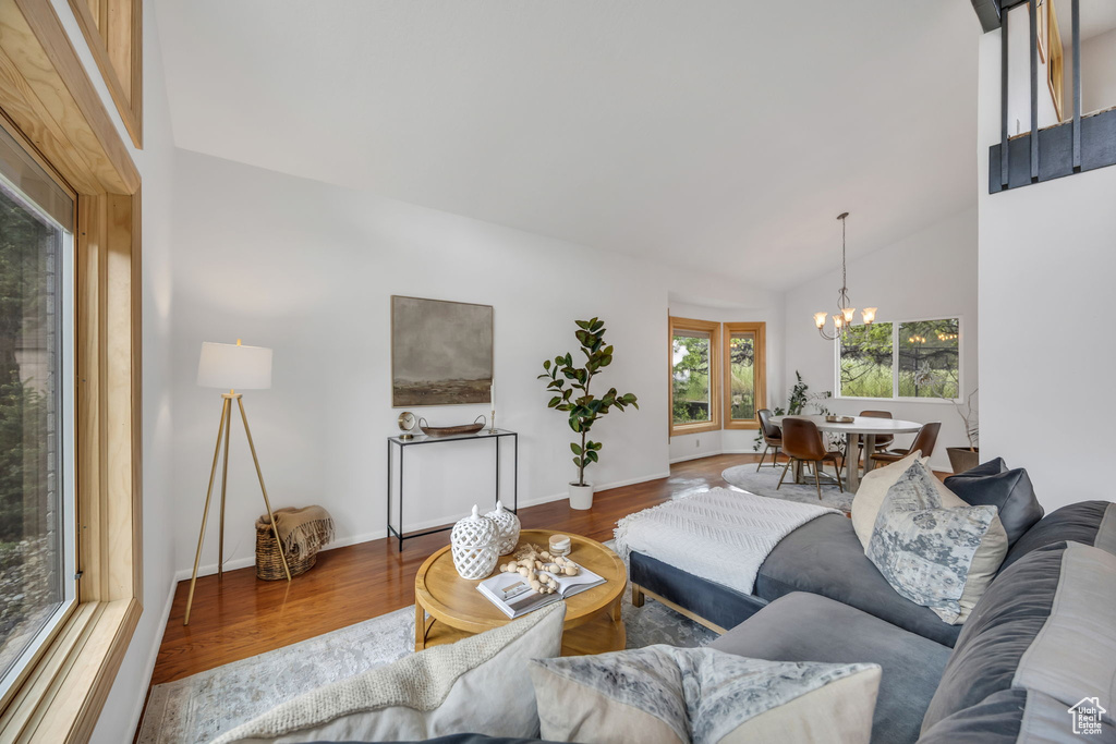 Living room with a chandelier, wood finished floors, vaulted ceiling, and baseboards