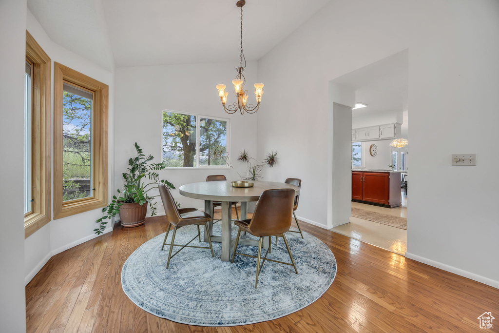 Dining area with vaulted ceiling, a chandelier, light wood-style floors, and baseboards