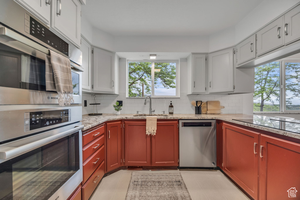 Kitchen featuring appliances with stainless steel finishes, a sink, backsplash, and light stone countertops