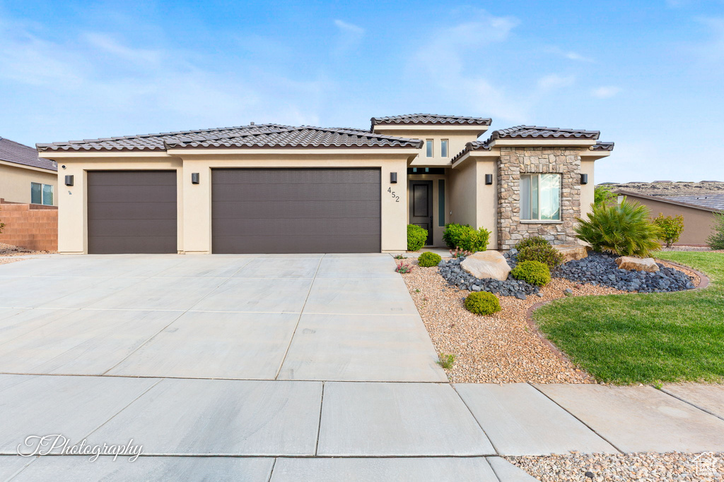 View of front of house featuring stucco siding, a garage, driveway, a tile roof, and stone siding