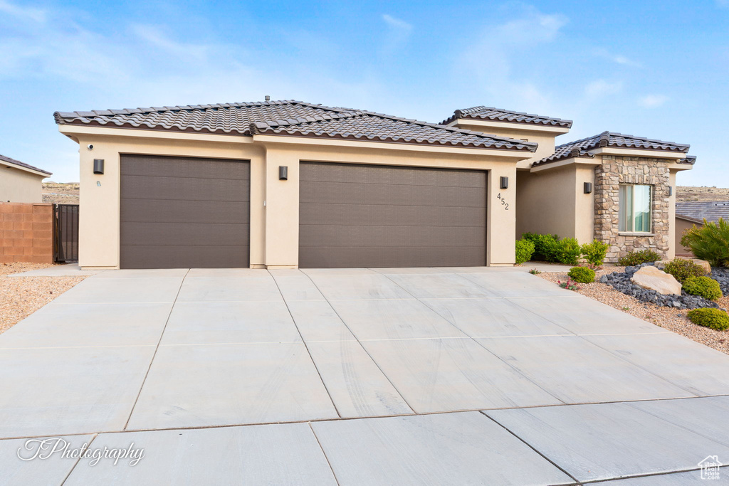 View of front of home featuring an attached garage, stucco siding, concrete driveway, fence, and a tiled roof
