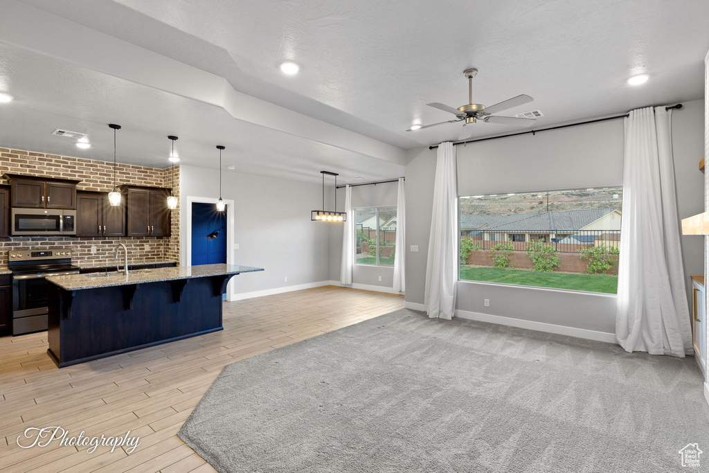 Kitchen with stainless steel appliances, a kitchen bar, ceiling fan, dark brown cabinets, and a kitchen island with sink