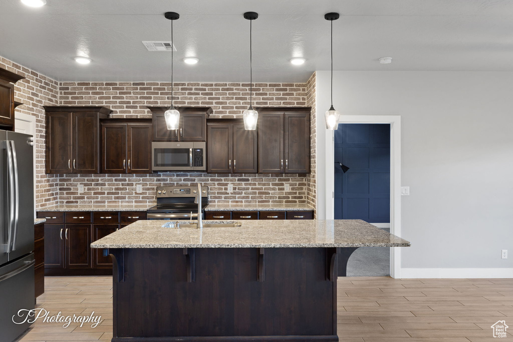 Kitchen featuring appliances with stainless steel finishes, a sink, a breakfast bar area, light wood-style floors, and dark brown cabinets
