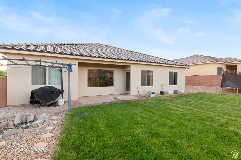 Back of property with a trampoline, stucco siding, a tiled roof, a patio, and a pergola