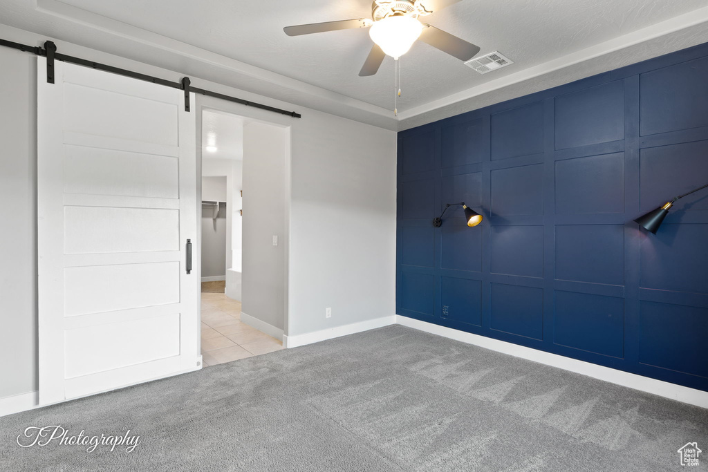 Tiled spare room featuring carpet flooring, a ceiling fan, a barn door, and a tray ceiling