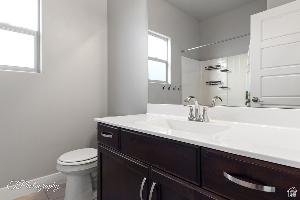 Full bathroom featuring toilet, tile patterned flooring, vanity, baseboards, and a shower