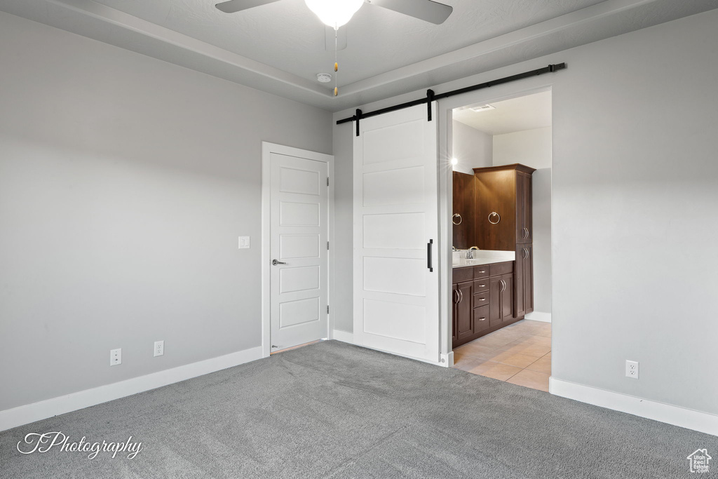 Unfurnished bedroom with a barn door, light colored carpet, baseboards, connected bathroom, and a sink