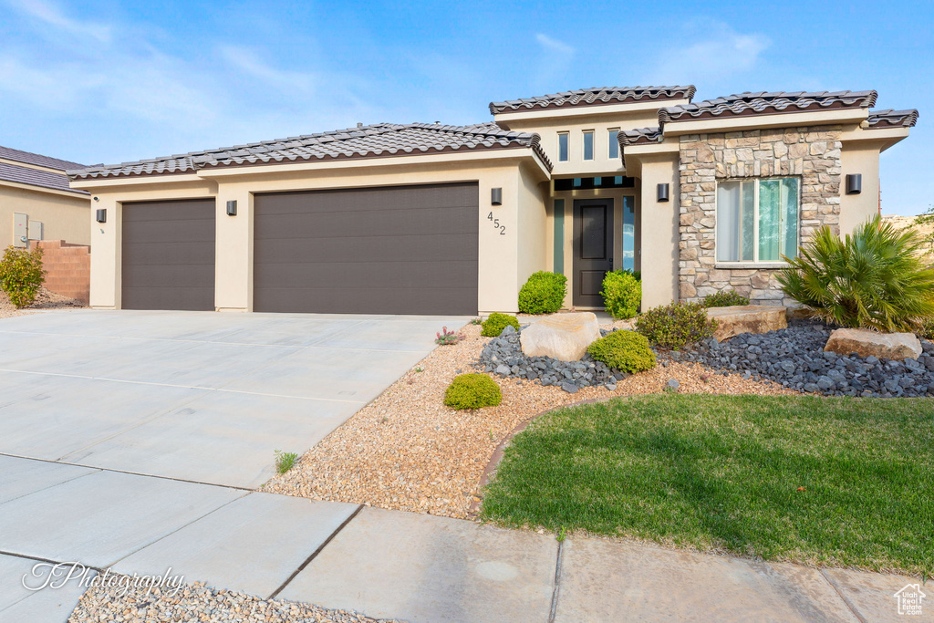 View of front facade featuring stucco siding, a garage, driveway, stone siding, and a tiled roof