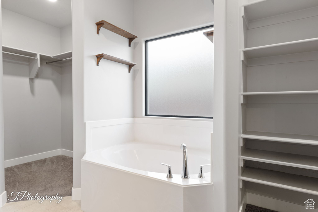 Bathroom featuring a walk in closet, a garden tub, and tile patterned floors