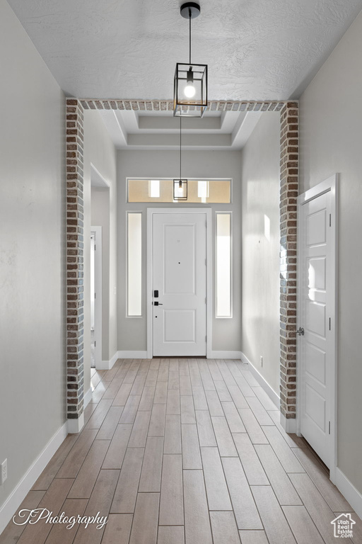 Foyer entrance with a raised ceiling, baseboards, light wood-type flooring, and a textured ceiling