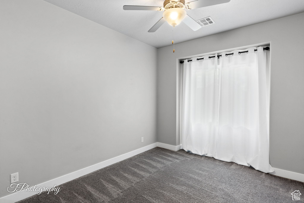 Empty room with dark carpet, baseboards, and ceiling fan