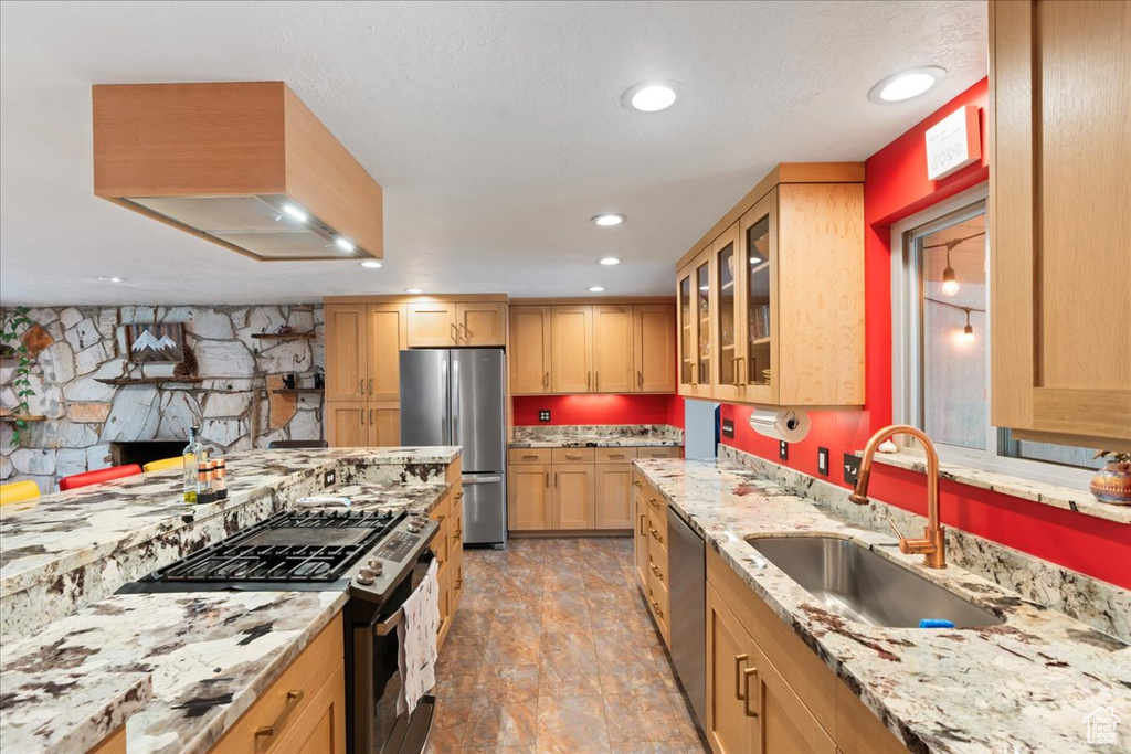 Kitchen featuring appliances with stainless steel finishes, a sink, light stone countertops, glass insert cabinets, and light brown cabinetry