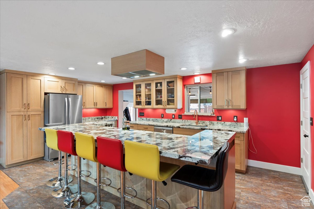 Kitchen featuring a sink, appliances with stainless steel finishes, a kitchen island, baseboards, and a breakfast bar area